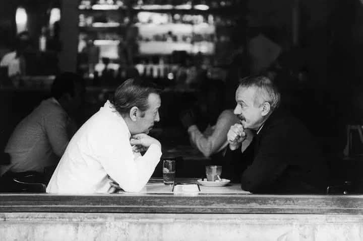 Astor Piazzolla · Roberto Goyeneche — Roberto Goyeneche y Astor Piazzolla en un bar porteño en los años 80, charlando sentados a una mesa junto al ventanal.